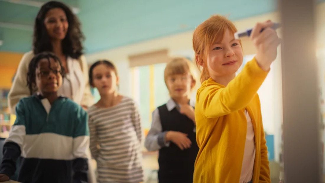 A diverse group of children in front of a whiteboard, actively involved in a classroom discussion.